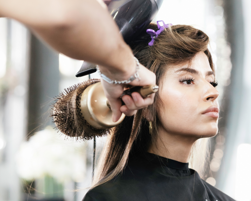Stylist föhnt einer Kundin die Haare zu einem voluminösen Blowout im Friseursalon in Wien
